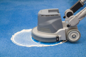Chemisches Schäumen, Reiben und Reinigen eines blauen Teppichs mit einer professionellen Scheiben-Reinigungsmaschine.