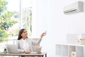 Junge Frau mit Fernbedienung der Klimaanlage im Büro.